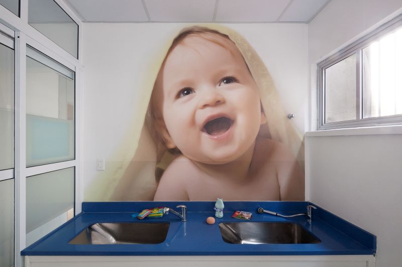 Fraldário em espaço escolar com foto de bebê na parede.